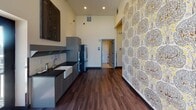 Located in the heart of Saint Paul, MN, this single-floor space offers a thoughtfully designed interior that blends modern functionality with distinctive aesthetic touches. The open layout is anchored by soaring ceilings and large clerestory windows that flood the interior with natural light, creating an airy and welcoming atmosphere throughout.

The kitchen is a standout feature, outfitted with gray shaker-style cabinetry, a classic farmhouse sink, stainless steel appliances including a French door refrigerator, built-in microwave, and double wall oven. Dark wood-look flooring runs throughout the space, providing a warm contrast to the light-toned walls.

A bold, nature-inspired wallpaper accent wall adds an artistic focal point, lending personality and visual depth to the main living corridor. The open living and gathering area features a central butcher block island with seating, bathed in sunlight from large glass doors that open to an outdoor area, offering seamless indoor-outdoor connectivity.

The bathroom is designed with accessibility in mind, featuring white subway tile walling, classic black-and-white patterned mosaic floor tile, and sturdy grab bars throughout. The overall ambiance of the space is bright, modern, and versatile, making it well-suited for a variety of uses.