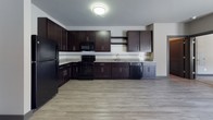 Located at 10501 Landing Way in Miamisburg, Ohio, this single-floor residence offers a cohesive modern design throughout. The interior is finished with a neutral gray color palette, dark baseboards, and dark-trimmed doors that create a clean, contemporary aesthetic. Living areas feature durable wood-look luxury vinyl plank flooring, while the bedrooms are fitted with plush carpeting for added comfort. Natural light flows through multiple windows dressed with horizontal blinds, and select rooms benefit from direct outdoor access via French doors. The kitchen is a standout feature, showcasing rich dark espresso cabinetry, granite-style countertops, a subway tile backsplash, and a full suite of black appliances including a refrigerator, range, microwave, and dishwasher. The bedrooms are generously sized, each offering ample wall space and closet access. The bathroom includes a shower/tub combination with clean white fixtures and a vanity with dark cabinetry. A dedicated in-unit laundry room provides side-by-side washer and dryer units with wire shelving above for additional storage. The layout is functional and efficient, making this a well-appointed space suited for comfortable everyday living.