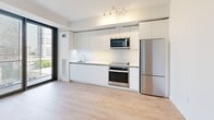 Located at 707 Terry Ave in Seattle's First Hill neighborhood, this modern one-bedroom, one-bathroom residence offers a thoughtfully designed single-level layout. Throughout the space, light wood-tone flooring and crisp white walls create a clean, contemporary aesthetic that maximizes the sense of openness.

The kitchen is a standout feature, showcasing a full wall of flat-front white cabinetry extending to the ceiling for ample storage. Stainless steel appliances — including a refrigerator, oven, over-the-range microwave, and a smooth-top range — are complemented by a streamlined countertop and recessed track lighting above. Large windows along one wall invite abundant natural light and views of the surrounding cityscape.

The bedroom is a well-proportioned retreat featuring light wood flooring and direct access to a dedicated closet. A floor-to-ceiling glass door opens to a private outdoor space framed by an exposed concrete column, adding an industrial-modern architectural accent. Two connecting hallways provide a smooth flow through the unit, enhancing functionality.

The bathroom is finished with a modern floating vanity with an integrated sink, recessed lighting, and light tile flooring. The overall design of this residence is clean, minimal, and well-appointed, making it an ideal urban home in the heart of Seattle.