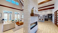 Located at 19216 Dr John Lambert Dr in Hammond, Louisiana, this thoughtfully designed single-floor space blends modern sophistication with warm, rustic touches throughout its open-concept layout. The most commanding architectural feature is the dramatic vaulted ceiling, accentuated by rich, dark wood exposed beams that draw the eye upward and create a grand sense of vertical space. Light wood-look tile flooring runs seamlessly throughout, complementing the neutral color palette and enhancing the airy ambiance.

At the heart of the space stands a striking floor-to-ceiling textured tile fireplace surround, complete with a chunky reclaimed wood mantel and a sleek linear gas fireplace. This centerpiece serves as a natural divider between the living and kitchen areas while remaining visually open on both sides. A living green wall adds an unexpected organic accent nearby, alongside glass-panel barn doors that lend a contemporary-rustic character.

The kitchen features rich cabinetry in both dark and slate-toned finishes, quartz countertops, stainless steel appliances, subway tile backsplash, open floating shelves, and a pendant globe chandelier. Large windows throughout flood the space with natural light and offer views of the surrounding exterior. A dedicated seating nook near the entrance provides a welcoming, conversational area, rounding out this versatile and well-appointed space.