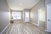This single-floor home offers a thoughtfully designed layout with a clean, contemporary aesthetic. The entryway welcomes visitors with light hardwood-style flooring, warm neutral-toned walls, and a front door with frosted glass panels that allow natural light to filter in. A large window near the entry further brightens the space and provides views of the surrounding neighborhood.

The living area is a standout feature, boasting soaring vaulted ceilings that create an impressive sense of openness and volume. The same light hardwood-style flooring continues throughout the main living spaces, lending a cohesive, airy feel.

The kitchen is well-equipped with rich dark wood cabinetry, granite-style countertops, and a full suite of stainless steel appliances including a range, microwave, and dishwasher. A window above the sink and a secondary exterior door offer additional natural light and convenient access.

The bedrooms are finished with plush wall-to-wall carpeting and feature large windows with blinds that allow for adjustable natural light. Ceiling fans provide added comfort. The bathroom is finished with matching dark wood cabinetry, a light countertop, and hardwood-style flooring, maintaining the home's consistent design language throughout.