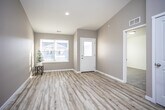 This single-floor home offers a thoughtfully designed layout with a clean, contemporary aesthetic. The entryway welcomes visitors with light hardwood-style flooring, warm neutral-toned walls, and a front door with frosted glass panels that allow natural light to filter in. A large window near the entry further brightens the space and provides views of the surrounding neighborhood.

The living area is a standout feature, boasting soaring vaulted ceilings that create an impressive sense of openness and volume. The same light hardwood-style flooring continues throughout the main living spaces, lending a cohesive, airy feel.

The kitchen is well-equipped with rich dark wood cabinetry, granite-style countertops, and a full suite of stainless steel appliances including a range, microwave, and dishwasher. A window above the sink and a secondary exterior door offer additional natural light and convenient access.

The bedrooms are finished with plush wall-to-wall carpeting and feature large windows with blinds that allow for adjustable natural light. Ceiling fans provide added comfort. The bathroom is finished with matching dark wood cabinetry, a light countertop, and hardwood-style flooring, maintaining the home's consistent design language throughout.