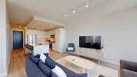 Located in Chicago's River North neighborhood, this high-rise residence offers a sleek, modern interior defined by an open-concept layout and an abundance of natural light. Floor-to-ceiling windows frame expansive, unobstructed views of the Chicago skyline and cityscape, creating a striking backdrop throughout the living spaces.

The open living and dining area flows seamlessly from the kitchen, with light hardwood flooring running throughout and track lighting overhead. The kitchen is outfitted with flat-front white cabinetry extending to the ceiling, a large center island with seating, light quartz countertops, and stainless steel appliances including a gas range, built-in microwave, and refrigerator. A dedicated dining area accommodates a full-sized table and sits adjacent to floor-to-ceiling windows.

The bedroom features panoramic city views through oversized windows on two walls, allowing generous natural light and dramatic skyline sightlines. The bathroom is finished with dark tile surrounds, a glass-enclosed walk-in shower with a rain showerhead, a white vanity with an illuminated mirror, and polished fixtures. The overall aesthetic is clean, minimalist, and contemporary throughout.
