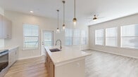 Located at 1951 Integra Dr in West Melbourne, FL, this well-designed 2-bedroom, 3-bathroom single-story home offers a bright, modern aesthetic throughout. The open-concept kitchen and living area serves as the heart of the home, anchored by a large center island with crisp white quartz countertops, a stainless steel sink, and three stylish pendant lights with brass accents. Light wood-style flooring flows through the main living areas, while multiple windows dressed with white blinds allow generous natural light to fill the space. A ceiling fan enhances comfort in the living room, which also benefits from direct access to an outdoor area via a glass-panel door. The bedrooms feature plush carpeting and well-sized windows with outdoor views, including glimpses of greenery and the surrounding neighborhood. The spacious primary bedroom includes a walk-in closet outfitted with wire shelving for organized storage. The bathrooms are finished with wood-look tile flooring, gray cabinetry, white countertops, and tile-surround fixtures — one featuring a soaking tub and shower combo, another with a standalone walk-in shower. The neutral color palette and clean finishes throughout create a cohesive, move-in-ready atmosphere.
