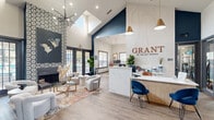 The Grant at Valley Ranch clubhouse is a thoughtfully designed single-story community space that blends modern aesthetics with functional amenities. Soaring vaulted ceilings and strategically placed skylights flood the interior with natural light, creating an open and airy atmosphere throughout.

At the heart of the space is a polished reception area, anchored by a sleek marble-topped desk with fluted wood paneling accents and paired with navy blue velvet chairs. Warm gold pendant lights hang above, complementing the natural wood-toned accent wall bearing the community's signature branding. Adjacent workstations are visible in the background, supporting the leasing and management functions of the space.

The lounge area is a standout feature, centered around a dramatic floor-to-ceiling fireplace wall clad in bold geometric patterned tile and adorned with a striking heron wall mural. Plush curved lounge chairs in soft grey tones are arranged around a glass coffee table atop a layered area rug, creating an inviting gathering space. Large French doors open directly to outdoor views of the pool area, seamlessly connecting interior and exterior living.

Wide-plank wood-look flooring runs throughout, tying the spaces together with a warm, cohesive feel. Deep navy accent walls provide rich contrast against crisp white ceilings and trim. A glass-enclosed fitness center is conveniently accessible from the reception area, offering residents a well-equipped workout space with abundant natural light.