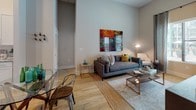 This single-floor residence is designed with a contemporary aesthetic, combining functional layouts with refined finishes. The kitchen is a standout space, outfitted with white shaker-style cabinetry extending to the ceiling, granite countertops, stainless steel appliances including a French door refrigerator, built-in microwave, and a gas range. Light hardwood flooring and a herringbone tile backsplash complete the polished look, while a gallery wall of framed camera photography adds a distinctive touch.

The living area features notably tall ceilings that amplify the sense of openness, with hardwood flooring continuing throughout. A dining area sits adjacent, creating a cohesive open flow between spaces.

The unit includes multiple bedrooms, each carpeted and furnished with windows that allow natural light. One bedroom connects directly to a private en-suite bathroom featuring granite countertops, a wide undermount sink, white cabinetry, and a large mirror. A second full bathroom mirrors this design, offering a double-sink vanity with ample counter space and white cabinetry.

Throughout, the neutral gray and white color palette creates a calm, cohesive ambiance, complemented by consistent granite surfaces and quality finishes that define the overall character of the residence.