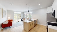 This thoughtfully designed two-bedroom, two-bathroom residence offers a bright and contemporary living experience across a single floor. The open-concept kitchen and living area serves as the heart of the home, anchored by a sleek center island with a white quartz countertop, an undermount sink, and pendant lighting overhead. Warm natural wood cabinetry pairs with white upper cabinets and a subway tile backsplash, while stainless steel appliances complete the modern aesthetic. Large picture windows flood the space with natural light and frame views of the surrounding neighborhood, seamlessly connecting the interior to the outdoors. Light hardwood flooring runs throughout, enhancing the airy, cohesive feel. The open living area provides generous space for both dining and lounging. Both bedrooms are well-proportioned, with the primary bedroom featuring floor-to-ceiling windows that bring in abundant natural light and street views. A dedicated closet offers walk-in style storage with wire shelving. A stacked washer and dryer is conveniently tucked into a closet off the main hallway. Two full bathrooms provide functional comfort, with clean tile finishes. Recessed lighting throughout maintains a clean, modern look across every room.