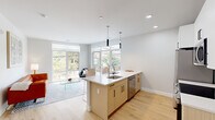 This thoughtfully designed two-bedroom, two-bathroom residence offers a bright and contemporary living experience across a single floor. The open-concept kitchen and living area serves as the heart of the home, anchored by a sleek center island with a white quartz countertop, an undermount sink, and pendant lighting overhead. Warm natural wood cabinetry pairs with white upper cabinets and a subway tile backsplash, while stainless steel appliances complete the modern aesthetic. Large picture windows flood the space with natural light and frame views of the surrounding neighborhood, seamlessly connecting the interior to the outdoors. Light hardwood flooring runs throughout, enhancing the airy, cohesive feel. The open living area provides generous space for both dining and lounging. Both bedrooms are well-proportioned, with the primary bedroom featuring floor-to-ceiling windows that bring in abundant natural light and street views. A dedicated closet offers walk-in style storage with wire shelving. A stacked washer and dryer is conveniently tucked into a closet off the main hallway. Two full bathrooms provide functional comfort, with clean tile finishes. Recessed lighting throughout maintains a clean, modern look across every room.
