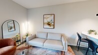 Located at 500 Maury Street in Richmond, Virginia, this modern one-bedroom, one-bathroom unit offers a thoughtfully designed layout across a single floor. The open-concept kitchen and living area serves as the heart of the home, featuring a sleek kitchen with white cabinetry, quartz countertops, stainless steel appliances including a refrigerator, range, and microwave, and a deep undermount sink. Polished concrete floors run throughout, adding an industrial-modern touch to the bright, neutral interiors. The living area is bathed in natural light through large sliding glass doors that open to an outdoor balcony, offering views of the surrounding Richmond cityscape. The bedroom is a comfortable retreat, complete with a ceiling fan, roller shade window treatments, and a window overlooking the balcony, allowing for additional natural light. The full bathroom features light tile flooring, a white vanity with an LED-backlit mirror, and a shower-tub combination. A dedicated laundry area houses a stacked Electrolux washer and dryer alongside built-in shelving for added storage. Clean lines, neutral tones, and modern fixtures create a cohesive and contemporary aesthetic throughout the entire space.