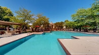 Located at 5489 Crescent Ridge Dr in Dublin, Ohio, this outdoor amenity space is designed to deliver a resort-style experience within a residential community setting. The centerpiece of the space is a generously sized swimming pool with a curved, free-form design, featuring brick-trimmed edges and multiple entry points via stainless steel handrails. The crystal-clear turquoise water is complemented by a broad surrounding pool deck finished in neutral concrete, providing ample room for lounging and socializing.

A dedicated sunbathing area lines one side of the pool, furnished with rows of chaise lounge chairs positioned beneath the shade of established mature trees that provide natural relief on sunny days. On the opposite side of the pool, a charming pergola structure serves as a shaded gathering spot, complete with outdoor seating and what appears to be a built-in grill or bar area, making it ideal for outdoor entertaining.

A separate outdoor lounge area features a centrally placed fire pit surrounded by additional seating, offering a cozy, intimate space for evening gatherings. The entire amenity area is enclosed by a decorative iron fence and is beautifully framed by lush, mature trees that provide both privacy and a scenic natural backdrop. A prominent brick-accented clubhouse building is visible adjacent to the pool, further enhancing the well-appointed character of this outdoor space.