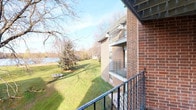 This single-floor residence offers a comfortable and functional layout designed to maximize both livability and natural scenery. The exterior is clad in classic brick, and a private balcony with wrought iron railings provides direct views of a lush green lawn and a tranquil body of water framed by mature trees — a standout feature that brings a sense of calm to everyday living.

Inside, the living room serves as the heart of the home, featuring neutral carpet flooring, a textured ceiling, and a wall-mounted air conditioning unit. A large sliding glass door floods the room with natural light and opens directly onto the balcony, maintaining a seamless connection to the outdoor scenery. The space flows naturally into a dedicated dining area, which is brightened by a ceiling light fixture and accented with decorative wall art, creating an inviting atmosphere for meals.

The kitchen is efficiently designed with warm wood cabinetry lining both sides, offering generous storage throughout. White appliances — including a refrigerator, dishwasher, and range — complement the clean white countertops and light tile flooring, giving the kitchen a bright, practical feel.

Overall, this residence combines classic brick construction with comfortable interiors and exceptional outdoor views, making it an appealing and well-rounded living space.