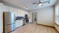 This single-floor residence is designed with a clean, contemporary aesthetic that carries throughout its well-organized layout. The kitchen serves as a functional centerpiece, outfitted with an extensive run of white shaker-style cabinetry that extends to the ceiling, providing generous storage. A full suite of stainless steel appliances includes a French door refrigerator, electric range with microwave above, and dishwasher, all complemented by a gray subway tile backsplash and a undermount sink. Track lighting illuminates the workspace, while light wood-look flooring extends seamlessly into the adjacent living area, which is fitted with a ceiling fan overhead.

A set of double doors provides access to additional storage or a closet near the kitchen. The bedroom is a well-proportioned, open room featuring two windows dressed with white blinds that bring in natural light and offer exterior views, along with its own ceiling fan. The bathroom is finished with large-format marble-style tile flooring, a dual-sink vanity with white cabinetry, and clean, neutral walls that create a bright, polished atmosphere throughout.