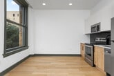 This thoughtfully designed studio offers a smart, open-concept layout that makes excellent use of its compact footprint. Light hardwood flooring flows continuously throughout the space, creating a warm and cohesive aesthetic enhanced by crisp white walls and dark-trimmed accents.

The living area is bright and open, benefiting from large, dark-framed windows that frame sweeping city views, allowing natural light to fill the room. A ceiling fan adds a functional touch to the airy atmosphere. An open closet with a built-in rod provides convenient storage within the living space.

The kitchen is well-appointed with a clean, contemporary design featuring two-tone cabinetry — warm wood lower cabinets paired with white upper cabinets — and a striking penny-tile backsplash in slate blue. Stainless steel appliances, including a range, microwave, and refrigerator, complement the white countertops and matte black hardware. A single-basin sink completes the functional layout.

The bathroom offers a polished, modern finish with a wood-toned vanity, white quartz countertop, and a full tub-shower combination clad in white subway tile. A bold charcoal accent wall and penny-tile flooring add visual depth and style.

The hallway provides a practical entry transition, housing the electrical panel and offering access to both the bathroom and main living area.