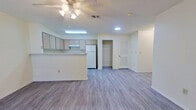 This 2-bedroom, 1-bathroom single-floor unit offers a functional and well-organized layout designed to maximize comfort and usability. The open-concept living and kitchen area forms the heart of the home, featuring durable grey vinyl plank flooring that flows seamlessly throughout. A ceiling fan with light fixture overhead provides both comfort and illumination, complementing the bright, neutral white walls that keep the space feeling clean and airy.

The kitchen is equipped with a peninsula-style breakfast bar that doubles as a divider between the kitchen and living area, offering additional prep and seating space. Light wood cabinetry lines the walls, providing ample storage, while a white refrigerator and electric range complete the appliance package. Overhead fluorescent lighting ensures the kitchen remains well-lit.

Both bedrooms are generously proportioned with large windows that invite natural light, continuing the same vinyl plank flooring found throughout the unit. The primary bedroom is notably spacious and includes dedicated closet access. Two closets in total offer practical storage solutions, including one walk-in style with wire shelving.

The bathroom features a full tub-shower combination with white subway-tile surround, a light wood vanity with storage below, a wall mirror with overhead vanity lighting, and vinyl plank flooring. The overall aesthetic is clean, neutral, and move-in ready.