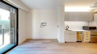 Located at 145 Leavenworth Street in San Francisco's Tenderloin neighborhood, this efficiently designed one-bedroom, one-bathroom unit offers a thoughtfully laid-out living space with clean, contemporary finishes throughout. Light wood-toned flooring runs across the entire unit, contributing to a bright and cohesive aesthetic.

The open living area flows directly into a streamlined kitchenette featuring white and light wood cabinetry, marble-look countertops, an undermount sink with a matte black faucet, and built-in appliances including a microwave. Upper cabinets with recessed lighting maximize storage without compromising the airy feel of the space. A large floor-to-ceiling sliding glass door fills the main area with natural light and provides views of the surrounding San Francisco streetscape.

The bedroom is served by a sliding barn-style door and includes a wall-mounted linear lighting fixture and a frosted-glass closet door, offering both functionality and a modern design touch. The bathroom is finished in crisp white tile and features an open walk-in shower with matte black grab bars and a rain-style showerhead, a wall-mounted sink, and a large mirror — all designed with accessibility in mind. The unit's minimalist design and efficient use of space make it a practical and stylish option in the heart of San Francisco.