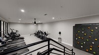 Located at 2124 Gables Dr NE in Atlanta, Georgia, this well-appointed fitness center offers a comprehensive exercise facility designed with both functionality and modern aesthetics in mind. The space is finished with neutral gray walls, crown molding, and durable low-pile carpet flooring throughout, creating a clean and professional atmosphere.

The main fitness floor is generously proportioned, housing an extensive lineup of TRUE-brand cardio equipment, including multiple treadmills, ellipticals, stair climbers, and stationary bikes, all arranged to maximize space and circulation. A large-blade ceiling fan ensures airflow across the workout floor, complemented by recessed lighting for bright, even illumination. A striking wall of black-framed glass panels lines one side of the room, allowing natural light to filter in while providing a sense of openness.

A standout feature of the facility is the built-in climbing wall — a Freedom Climber unit mounted against a dark accent wall — offering a unique and engaging training option. Adjacent to the climbing wall is a dedicated stretching and multi-use area with additional equipment including a rowing machine and cycle bike.

A split-level mezzanine area with sleek black railings adds a dynamic architectural element to the space, with additional cardio machines positioned on the upper level. The overall design is modern, functional, and well-equipped to support a wide range of fitness routines.
