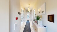 This thoughtfully designed single-floor amenity space offers a comprehensive suite of features catering to both recreation and everyday convenience. The entrance greets visitors with a bright, airy corridor finished in herringbone-patterned tile flooring, accented by a sleek runner and a modern globe pendant light fixture. A built-in reception console with decorative greenery sets a polished, welcoming tone.

The spacious lounge and game room serves as a social centerpiece, featuring rich hardwood floors, generous natural light streaming through multiple large windows, and a statement billiards table. Comfortable seating arrangements, including a sectional sofa and a round dining table with gold-accented chairs, make this area ideal for both casual gatherings and relaxed socializing. A sliding barn door with frosted glass panels adds a contemporary architectural touch.

The fitness center is generously proportioned and bathed in natural light from floor-to-ceiling windows on multiple walls. It is equipped with treadmills, ellipticals, stationary bikes, and a dedicated open floor area with exercise balls, medicine balls, and a wall-mounted television — well-suited for a variety of workout routines. A ceiling fan ensures comfortable airflow throughout.

The kitchen features dark espresso cabinetry, white quartz countertops, stainless steel appliances, and a striking mosaic tile backsplash, providing a fully functional space for food preparation and entertaining.