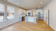 Located at 1601 Overbrook Rd in Richmond, VA, this contemporary two-floor residence showcases modern design and high-quality finishes throughout. The open-concept kitchen is a standout feature, equipped with stainless steel appliances, a central island, crisp white upper cabinetry, two-tone gray lower cabinets, quartz countertops, and a classic white subway tile backsplash — all set atop durable light wood-tone flooring that flows seamlessly through the home. Recessed lighting and large windows allow natural light to fill the kitchen and adjoining living areas. The living spaces are bright and airy, featuring ceiling fans and expansive windows with exterior views that bring the outdoors in. A door leads to a private balcony, offering additional outdoor access. The bathrooms are well-appointed; the primary bath includes a dual-sink vanity with quartz countertops and a glass-enclosed shower, while the secondary bath features a tiled tub-shower combo with hexagonal floor tile and brushed nickel fixtures. Multiple walk-in closets with wire shelving systems provide generous storage throughout the home. The light hardwood flooring, neutral color palette, and clean architectural lines give the entire space a bright, move-in-ready feel.