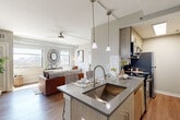 This thoughtfully designed one-bedroom, one-bathroom unit offers an efficient and stylish single-floor layout. The open-concept living and kitchen area forms the heart of the space, where warm hardwood-style flooring, exposed metallic ductwork, and neutral tones create a modern urban aesthetic. The kitchen is anchored by a central island with a stainless steel sink, gray quartz countertops, pendant lighting, and wood-toned upper cabinetry, complemented by stainless steel appliances including a gas range and microwave. Track lighting and ceiling fans add functional versatility throughout. The living room is bathed in natural light from large windows that frame impressive city skyline views, enhancing the open and airy feel of the space. The bedroom is a calm retreat, featuring a ceiling fan, a window with exterior views, and exposed ductwork that adds an industrial touch. A dedicated closet provides practical storage. The bathroom is finished with white subway tile in the walk-in shower with a sliding glass door, a wood-toned vanity with gray countertops, and hardwood-style flooring. Every detail in this unit reflects a cohesive modern design with urban character.