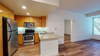 This single-floor residence offers a thoughtfully designed layout with clean lines, neutral tones, and consistent hardwood-style flooring that flows seamlessly throughout every room. The open-concept kitchen serves as the heart of the home, equipped with warm-toned wood cabinetry, stainless steel appliances including a gas range, microwave, and refrigerator, and a granite-topped peninsula that doubles as a breakfast bar. Recessed lighting illuminates the space, while under-cabinet lighting adds a refined touch to the kitchen's functionality.

The living area is open and inviting, connecting naturally to the kitchen and leading to the bedrooms via a central corridor. Each bedroom is bright and well-proportioned, featuring large windows with horizontal blinds that invite generous natural light and offer views of lush greenery outdoors. The clean white walls provide a versatile canvas for any interior style.

Two full bathrooms serve the residence, both finished with granite countertops and hardwood-style flooring. The primary bathroom includes a wide vanity with ample storage, a large mirror, and a tub-shower combination. The secondary bathroom is similarly appointed with a tub-shower unit in a crisp, all-white finish. Together, these spaces reflect a consistent commitment to clean, modern design throughout the home.