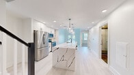 Located in the heart of Fredericksburg, VA, this thoughtfully designed two-floor residence at 606 Amelia St offers a seamless blend of modern elegance and functional living. The main level centers around a show-stopping open-concept kitchen and living area, where light hardwood flooring and soft blue-gray walls create a bright, airy atmosphere. The kitchen is anchored by an expansive waterfall-edge island clad in dramatic white marble with bold veining, illuminated by a trio of globe pendant lights. Crisp white cabinetry and a full suite of stainless steel appliances complete the culinary space. Natural light flows freely through large windows and a glass-panel door that opens to the outdoors. The upper level is accessed via a stylish staircase with a black-and-white balustrade and features light hardwood flooring in the landing and hallway. Carpeted bedrooms offer a cozy feel, each brightened by large windows with outdoor views and fitted with ceiling fans. The bathrooms are finished to a high standard, showcasing floor-to-ceiling marble-style tile, a freestanding soaking tub, a glass-enclosed walk-in shower with mosaic tile flooring, and matte black fixtures throughout — delivering a spa-like experience within the home.