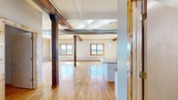 Located at 225 E 2nd St in downtown Davenport, Iowa, this 3-bedroom, 2-bathroom loft showcases a striking blend of historic industrial character and modern updates across a single, generously sized floor. The open-concept living and kitchen area is anchored by original hardwood floors, bold exposed timber columns and beams, and industrial-style ductwork that pays homage to the building's heritage. Multiple windows flood the space with natural light and frame captivating views of the waterfront. The kitchen features white shaker cabinetry, granite countertops and backsplash, stainless steel appliances, and a large island — all complemented by the rustic warmth of the surrounding hardwood floors and timber accents. The bedrooms offer a mix of exposed brick accent walls, hardwood flooring, and windows with views of the river and surrounding cityscape. The spacious primary bedroom provides ample room to relax. The bathrooms are finished with neutral tile flooring, clean white vanities, and modern fixtures. Throughout the space, the combination of whitewashed and natural brick walls, warm wood tones, and soaring ceilings creates an inviting industrial-chic ambiance unique to this downtown riverfront location.