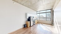 Located in the heart of downtown San Diego, this single-floor loft-style unit at 1009 G St offers a compelling blend of industrial design and modern functionality. The open-plan living and kitchen area is immediately defined by its exposed concrete ceiling, which lends a raw, urban character to the space while also contributing to a generous sense of vertical height. Warm hardwood flooring runs throughout, providing a striking contrast to the industrial overhead elements.

The kitchen is positioned along one wall and features stainless steel appliances — including a refrigerator, range, and microwave — complemented by light wood cabinetry, granite countertops, and white upper cabinets. A wall of large, floor-to-ceiling windows floods the living area with abundant natural light and offers open city views, further enhancing the airy feel of the space.

The bedroom is a well-proportioned room with the same hardwood flooring, exposed concrete ceiling details, and an open closet with built-in rod. A hallway connects the main living area to the bathroom and a dedicated in-unit laundry closet equipped with a stacked washer and dryer. The bathroom features a granite-topped vanity with wood cabinetry and a full tub-shower combination with tiled surround. Throughout, the unit maintains a clean, minimalist aesthetic suited to urban living.