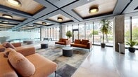 Located at 235 Rue Young in Montréal's dynamic Griffin Town neighbourhood, this expansive single-floor commercial space offers a thoughtfully designed contemporary work environment. The open-plan layout is anchored by polished concrete floors that run throughout, reflecting abundant natural light that pours in through expansive floor-to-ceiling glazed facades on multiple sides of the floor plate.

The space is organized into several distinct functional zones. A welcoming lounge area features warm terracotta-toned sofas, layered area rugs, and a striking coffered ceiling with inset natural wood panels and statement pendant lighting. An adjacent collaboration zone provides flexible seating arrangements suited for informal meetings and group work.

A sleek, fully equipped kitchen and bar area showcases crisp white cabinetry, a dark-topped island with bar seating, and warm wood ceiling accents — ideal for team gatherings. Multiple glass-walled private meeting rooms offer transparency and acoustic separation without sacrificing the open feel of the floor.

A bright, windowed boardroom accommodates large-format meetings, while perimeter workspaces overlook a landscaped outdoor terrace and the Montréal city skyline. Exposed concrete columns and structural elements add an industrial character that complements the refined, modern interior finishes throughout.
