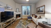 The Elevation floor plan at Bear Run Point in Colorado Springs, CO presents a thoughtfully designed one-bedroom, two-bathroom residence that maximizes its well-proportioned single-floor layout. The open-concept living and kitchen area creates a seamless flow, anchored by rich hardwood-style flooring that extends throughout the main living spaces. The kitchen is a standout feature, boasting dark espresso cabinetry, granite countertops, a subway tile backsplash, a center island with bar seating, and a full suite of stainless steel appliances including a refrigerator with ice maker, dishwasher, range, and microwave. Pendant lighting above the island adds a refined touch. The adjacent living room offers a cozy electric fireplace and a large window that fills the space with natural light. The bedroom is carpeted for comfort, features a ceiling fan, and is served by a generous walk-in closet with wire shelving. Both bathrooms are finished with granite-topped vanities and dark cabinetry consistent with the rest of the home. A dedicated laundry room houses full-size washer and dryer units. Neutral wall tones and clean architectural lines throughout give this residence a calm, contemporary ambiance suited for Colorado living.