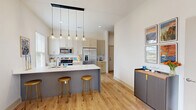Located at 1956 Sparrowstar Way in Ocean Isle Beach, NC, this two-story home offers a thoughtfully designed layout spread across two floors. The main level hosts the majority of the living space, including an open-concept area that seamlessly combines the living room, dining room, and kitchen. The kitchen is outfitted with slate-blue cabinetry, brass hardware, a large white quartz island with an undermount sink, and a striking row of pendant lights — all complemented by light hardwood flooring that flows throughout the home. The bright living area features tall ceilings, a glass door that invites natural light, and a welcoming coastal ambiance. Three well-appointed bathrooms include clean, floor-to-ceiling white tile showers with built-in shelving. The generously sized primary bedroom offers a calm, airy atmosphere with ample natural light. Four closets, including a walk-in with full wire shelving systems, provide excellent storage. A dedicated laundry room, utility room with water heater, and an attached garage with an electrical panel add everyday convenience. The upper floor provides additional flexible space. Outside, a concrete driveway leads to the garage, and the property enjoys tranquil views of a neighboring pond framed by native landscaping.