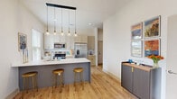 Located at 1956 Sparrowstar Way in Ocean Isle Beach, NC, this two-story home offers a thoughtfully designed layout spread across two floors. The main level hosts the majority of the living space, including an open-concept area that seamlessly combines the living room, dining room, and kitchen. The kitchen is outfitted with slate-blue cabinetry, brass hardware, a large white quartz island with an undermount sink, and a striking row of pendant lights — all complemented by light hardwood flooring that flows throughout the home. The bright living area features tall ceilings, a glass door that invites natural light, and a welcoming coastal ambiance. Three well-appointed bathrooms include clean, floor-to-ceiling white tile showers with built-in shelving. The generously sized primary bedroom offers a calm, airy atmosphere with ample natural light. Four closets, including a walk-in with full wire shelving systems, provide excellent storage. A dedicated laundry room, utility room with water heater, and an attached garage with an electrical panel add everyday convenience. The upper floor provides additional flexible space. Outside, a concrete driveway leads to the garage, and the property enjoys tranquil views of a neighboring pond framed by native landscaping.