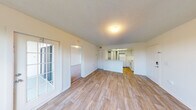 This single-floor unit offers a clean, functional layout designed for comfortable everyday living. The main living area is finished with light wood-style flooring that extends throughout, creating a cohesive and airy feel. Neutral white walls and a textured ceiling reflect natural light effectively, enhancing the sense of openness. A French-style door leads to an outdoor balcony area, allowing natural light to pour into the living space.

The kitchen is positioned adjacent to the living area, separated by a half-wall pass-through counter that maintains an open connection between the two spaces. White cabinetry, light countertops, and white appliances including an electric range with overhead ventilation give the kitchen a tidy, uniform appearance.

The bedroom is carpeted in a neutral tone, offering a softer underfoot feel and a quiet, restful atmosphere. A closet with bi-fold doors provides organized storage within the room.

The bathroom is straightforward and well-maintained, featuring an all-white walk-in shower stall with built-in shelving, a toilet, and a grab bar, presenting a clean and practical design. The unit also includes a dedicated entry door with a modern smart lock, adding a layer of convenience and security to the space overall.