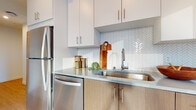 This contemporary single-floor residence is thoughtfully designed with a clean, modern aesthetic throughout. The kitchen is a standout feature, equipped with stainless steel appliances including a gas range, built-in microwave, and refrigerator. Warm wood-toned lower cabinetry is paired with crisp white upper cabinets, complemented by a striking white herringbone tile backsplash and smooth grey countertops. A deep stainless steel sink with a high-arc faucet adds both style and functionality.

The space includes two bathrooms. One features a full tub-shower combination with a curved curtain rod, warm wood vanity, and neutral tile flooring. The second offers a sleek undermount sink set in a white quartz countertop, a large mirror, and light wood cabinetry, creating a clean and airy feel.

The living area is bathed in natural light from expansive floor-to-ceiling windows that frame striking urban skyline views. Light hardwood flooring extends through the main living spaces. The bedroom continues the skyline views through large windows with plush carpet underfoot. An additional carpeted room, currently arranged as a home office, also benefits from generous natural light and city views, offering versatile functionality.
