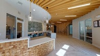 The Monterosso amenity center is a thoughtfully designed single-floor facility offering a comprehensive range of community spaces. The welcoming lobby greets visitors with a striking textured wood reception desk, slatted wood ceiling details, pendant globe lighting, and a bold botanical feature wall displaying the Monterosso branding. Light hardwood flooring in a herringbone pattern extends throughout, unifying the space.

The clubroom lounge features floor-to-ceiling windows overlooking a resort-style pool area, a bar-height counter with stylish seating, pendant lighting, and accent artwork. Adjacent to it, a fully equipped social kitchen showcases a white quartz island with blue upholstered bar stools, an eye-catching geometric gold-and-white tile backsplash, and an illuminated wood-paneled ceiling.

The game room provides entertainment with a billiards table, ping pong table, wall-mounted televisions, and light hardwood flooring. Intimate dining nooks with large windows offer serene garden views. The fitness center is expansive and well-lit by large windows framing palm tree and pool views, housing cardio machines, free weights, strength equipment, floor mirrors, and a dedicated stretching area. Hallways connecting all areas are clean and bright, accented with decorative artwork throughout.