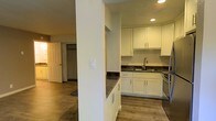 This single-floor residence offers a clean, modern aesthetic with thoughtful design details throughout. The kitchen is a standout feature, showcasing crisp white shaker-style cabinetry paired with rich dark countertops that create a striking contrast. A stainless steel sink and fixtures add a contemporary touch, while recessed lighting illuminates the space efficiently. The kitchen flows naturally into the surrounding living areas, creating an open and connected feel. A structural column provides subtle architectural definition between spaces without interrupting the open layout. Warm hardwood-style flooring runs throughout, lending a cohesive and inviting ambiance to the entire residence. Adjacent to the main living areas, a spacious closet with a hanging rod offers practical storage solutions. The neutral color palette of whites and warm wood tones creates a bright, airy atmosphere that feels both comfortable and functional. The layout is well-organized, making efficient use of the available space while maintaining a sense of openness. Overall, this residence combines practical amenities with modern finishes to deliver a clean, move-in-ready living environment.