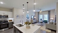 This single-floor residence is designed with a contemporary aesthetic, combining functionality and style across its open layout. The kitchen serves as a central focal point, featuring a large island with a white quartz countertop, a single-basin sink with a high-arc faucet, and pendant lighting overhead. Cabinetry is finished in a two-tone scheme of white upper cabinets and dark gray lower cabinets, complemented by a white subway tile backsplash and stainless steel appliances, including a refrigerator, range, and built-in microwave.

The kitchen flows seamlessly into the living area, where wood-look flooring, a ceiling fan, and French doors provide access to an outdoor space, filling the room with natural light and outdoor views. The bedrooms are carpeted and well-lit by large windows, each equipped with a ceiling fan. One bedroom features an en-suite bathroom with a walk-in glass shower, a dual-sink vanity with dark cabinetry and white countertops, wood-look flooring, and direct access to a spacious walk-in closet. A second bathroom offers a similar vanity configuration with walk-in closet access. Throughout, the neutral color palette and consistent finishes create a cohesive, polished ambiance.
