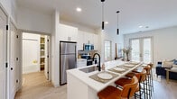 Located at 6220 Guilford Ave in Indianapolis, Indiana, this well-designed one-bedroom, one-bathroom unit offers a thoughtful layout across a single floor. The open-concept kitchen and living area serves as the heart of the home, anchored by a large white waterfall island with bar seating for four, illuminated by sleek pendant lighting. The kitchen is equipped with stainless steel appliances, including a refrigerator, electric range, and microwave, complemented by tall white cabinetry that maximizes storage. Light wood-look flooring flows throughout the main living areas, enhancing the bright, airy atmosphere created by recessed lighting and large windows. The living room opens to a private balcony through glass French doors, filling the space with natural light and outdoor views. The bedroom is a comfortable retreat featuring plush carpeting, a ceiling fan, and a generously sized window overlooking greenery. A barn-style door leads toward the bathroom, which includes a tiled tub-shower combination and wood-look flooring. Two closets provide ample storage, and a dedicated laundry area houses a stacked washer and dryer unit for added convenience. Clean white walls and modern finishes throughout give this space a cohesive, contemporary feel.