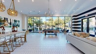 This thoughtfully designed single-floor amenity space blends modern aesthetics with functional comfort across several distinct areas. The reception entry makes an immediate impression with a striking textured front desk, herringbone-patterned tile flooring, a sculptural sarburst chandelier, and glass-paneled doors that lead deeper into the space.

The centerpiece of the facility is a generously sized game and lounge area, anchored by a full-size billiards table and finished with white hexagonal tile floors. Floor-to-ceiling black-framed windows span the entire rear wall, flooding the room with natural light and offering expansive views of an outdoor pool and tree-lined grounds beyond. A circular chandelier hangs overhead, while modular seating, bar-height tables, and accent chairs are thoughtfully arranged throughout.

A media lounge area features bold black-and-white horizontal striped walls, a wall-mounted flat-screen TV above a textured floating cabinet, and an eclectic mix of contemporary furnishings with gold-toned accents — creating a vibrant, social atmosphere.

The kitchenette is a design standout, showcasing an ornate gold-and-silver ogee mosaic tile backsplash, dark countertops, a beverage refrigerator, oven, and a brass faucet — all framed by textured cabinetry.

A cozy lounge nook offers a more intimate retreat, with a blush velvet daybed, teal ottomans, gold leaf wall art, and a full-length mirror. Private office or meeting rooms with glass walls line the corridor, completing this multifaceted community space.