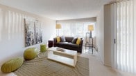 This single-floor residence offers a thoughtfully organized layout with a variety of functional living spaces. The living room serves as the central gathering area, featuring large vertical-blind windows that flood the room with natural light, neutral carpet flooring, and a textured ceiling. A separate sitting room provides a quieter retreat, accented with warm leather armchairs and decorative wall art. The galley-style kitchen is efficiently designed with warm wood cabinetry, white countertops, a classic black-and-white checkered tile floor, and black appliances including a full-sized refrigerator and dishwasher. A pass-through connects the kitchen to the rest of the living areas, enhancing the sense of flow throughout the unit. The bedroom is generously sized, featuring plush carpet, a wide window with vertical blinds offering ample natural light, a baseboard heating unit, and a wall-mounted air conditioning unit. A hallway leads to two full bathrooms positioned side by side, each outfitted with tile flooring, a pedestal sink, vanity lighting, and clean, neutral finishes. Together, these spaces create a comfortable and practical living environment with a calm, neutral aesthetic throughout.