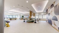 Located at 345 St Peter St in downtown Saint Paul, Minnesota, this sophisticated commercial lobby offers a refined and welcoming first impression. The single-floor space is generously proportioned, with soaring ceilings that amplify the sense of openness and grandeur. Floor-to-ceiling glass curtain walls flood the interior with abundant natural light while framing views of the surrounding urban streetscape, and a polished brass revolving entry door serves as a striking architectural focal point at the main entrance.

The flooring transitions elegantly between light travertine-toned stone in the main lobby and richly veined dark marble in the elevator corridor, delineating distinct zones within the space. A sculptural reception desk finished in dramatic blue-grey marble commands attention near the elevator bank, complemented by warm ambient underlighting. Overhead, contemporary ring-shaped pendant light fixtures add a modern artistic element against the crisp white ceiling.

A curved, jewel-toned sectional sofa in deep rose and burgundy anchors the seating lounge, paired with minimalist side tables in black and marble. Toward the rear, an ornate elevator lobby corridor features arched architectural detailing, decorative greenery, and refined wall treatments. A digital display panel is mounted flush to a warm wood-toned wall, adding a functional modern touch. The overall ambiance is polished, contemporary, and professional.