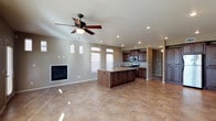 This two-story home showcases an open-concept main living area that seamlessly integrates the kitchen, dining, and living spaces into one cohesive layout. The living area features a built-in fireplace flanked by clerestory windows that allow natural light to filter in from multiple angles, complementing the recessed lighting and a ceiling fan with a light fixture overhead. The neutral-toned walls and textured ceiling create a warm, understated backdrop throughout.

The kitchen is anchored by a substantial dark wood island with granite countertops and an undermount sink, providing both prep space and a natural gathering point. Rich, dark cabinetry lines the kitchen walls and is paired with stainless steel appliances, including a microwave and range. The flooring throughout the main level consists of large-format polished tile in warm earth tones, adding to the sense of spaciousness. A hallway visible beyond the kitchen suggests additional rooms, while architectural columns subtly define the transition between spaces. Overall, the home presents a functional, well-lit, and cohesive interior with quality finishes throughout.