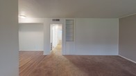 This single-story home presents a straightforward and functional layout designed for comfortable everyday living. The living area is generously sized, featuring wall-to-wall carpet, a textured ceiling, and a wide set of windows fitted with blinds that invite natural light while maintaining privacy. An accent wall with vertical paneling adds a subtle textural detail to the space. Adjacent to the living area, built-in shelving provides convenient storage and display options, seamlessly integrated into the wall.

The kitchen is equipped with an electric range, a range hood, light-toned laminate countertops, and a single-basin sink. White cabinetry lines the upper walls, offering ample storage. A window above the counter area allows for natural light and ventilation.

The bedrooms are carpeted and bright, each featuring ceiling fans with integrated light fixtures and windows with blinds. The rooms offer a clean, neutral palette ideal for a variety of uses.

The bathroom includes a full tub-and-shower combo surrounded by classic white square tile, complemented by a vanity area with a built-in countertop surface and Hollywood-style lighting. A separate closeted space adds additional storage. Hardwood-style flooring appears in transitional areas, providing a warm contrast to the carpeted rooms throughout the home.