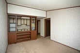Located in Chesterfield, MI, this single-floor property offers a straightforward and functional layout suited for comfortable everyday living. The living area is generously sized, featuring neutral-toned carpet flooring, textured wallpaper with a subtle pattern, and dark wood baseboards and crown molding that frame the space with a classic touch. A large window dressed with vertical blinds allows natural light to fill the room, while a front entry door provides a welcoming focal point. An additional carpeted room mirrors similar finishes, complete with a wall-mounted HVAC vent and a window overlooking the outdoors. The kitchen is equipped with white cabinetry accented by dark wood trim, offering ample upper and lower cabinet storage. White appliances — including a refrigerator, electric range, and overhead ventilation hood — complement the light parquet-style flooring. A single-basin sink sits beneath the countertop, completing the practical setup. The bathroom features a single-sink vanity with wood-trimmed cabinetry, a mirror cabinet above, a toilet, and a full-size tub and shower combo. Light tile flooring and cream-toned walls give the bathroom a clean, utilitarian appearance. Throughout the property, the consistent use of neutral tones and wood accents creates a cohesive, understated aesthetic.