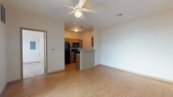 This single-story residence is designed with a practical, open-concept layout that connects the living area directly to the kitchen. The living space features light wood-style flooring and a ceiling fan with integrated lighting. A sliding glass door allows natural light to fill the room and provides outdoor views. The kitchen is positioned adjacent to the living area and is separated by a peninsula-style breakfast bar with beadboard detailing and a stone-look countertop. The kitchen itself is laid out in a galley configuration, equipped with medium-toned wood cabinetry, granite-style countertops, black appliances including a refrigerator, range, built-in microwave, and dishwasher, along with a pendant light fixture overhead.

The two bedrooms feature soft carpeting and large windows fitted with blinds that offer views of the surrounding area, providing ample natural light. The bathrooms include wood-style flooring, warm wood vanity cabinetry, and a full tub-shower combination. A dedicated laundry area houses a full-sized side-by-side washer and dryer with overhead wire shelving for additional storage. Neutral wall tones and consistent finishes create a cohesive, functional ambiance throughout the space.