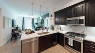 Located at 1961 E Dyer Rd in Santa Ana, CA, this thoughtfully designed single-floor residence showcases a curated blend of bold aesthetics and refined finishes throughout. The open-concept kitchen serves as a central hub, outfitted with rich dark cabinetry, white quartz countertops, a marble-inspired tile backsplash, and a full suite of stainless steel appliances including a gas range and French door refrigerator. Pendant lighting above the kitchen island adds warmth, while light wood-style flooring extends seamlessly into the living areas. The bedrooms are each distinctly styled, featuring striking botanical wallcoverings — from dramatic tropical banana leaf prints in deep greens to bold black-and-white palm frond patterns — creating a lush, resort-inspired atmosphere. Large windows and sliding glass doors invite natural light and offer views of the surrounding exterior. The bathrooms are finished with marble-look tile on floors and walls. One bathroom features a walk-in glass-enclosed shower with a rainfall showerhead and a built-in bench, while another includes a soaking tub-shower combo with a dark vanity and large mirror. An intimate outdoor patio provides additional space for relaxation.