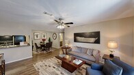 This single-floor, 2-bedroom, 2-bathroom home in Garden City, Georgia offers a functional and comfortable layout designed to maximize everyday living. The open-concept living and dining area features warm wood-style flooring, neutral-toned walls, and a ceiling fan with light fixture, creating a bright and inviting atmosphere. The living room flows seamlessly into the dedicated dining space, which is defined by a textured ceiling and connects directly to the kitchen. The galley-style kitchen is equipped with gray cabinetry, granite-look countertops, a double sink, and black appliances including a range and refrigerator, with a pass-through view into the dining area. The spacious primary bedroom features plush carpeting, a ceiling fan, a window with natural light, and a mirrored closet. The second bedroom is equally comfortable, with carpeted flooring, a ceiling fan, and natural light. Both bathrooms are finished with dark vanity cabinetry, granite-look countertops, large mirrors, wood-style tile flooring, and full tub-shower combinations. A dedicated laundry area accommodates a full-size side-by-side washer and dryer with overhead shelving for additional storage. Throughout the home, consistent finishes and neutral tones create a cohesive, move-in-ready aesthetic.