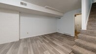 Located at 8900 W 102nd Ter in Overland Park, Kansas, this multi-level home spans three floors and offers a practical, well-organized layout. The main living level features a spacious carpeted living room accented by a striking exposed brick column, lending the space a distinctive character. Staircases connect each floor, providing easy access throughout the home. The combined kitchen and dining area is equipped with crisp white cabinetry, light granite-style countertops, a peninsula, and black appliances including a range and dishwasher, all set on wood-look flooring. An adjoining dining and living area offers additional flexible space with the same clean flooring. The upper floor houses two bedrooms, including a generously sized primary bedroom, along with multiple closets providing ample storage. Three bathrooms are distributed throughout the home, each finished with wood-look flooring and clean white fixtures. The lower level includes an unfinished basement with concrete floors and exposed wooden joists, offering significant storage or potential utility space, alongside a utility room and an attached garage with an automatic opener. The home's layout across each well-proportioned floor ensures a functional flow, making it a versatile and comfortable residence.