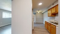 This single-story space is thoughtfully laid out across an open, flowing floor plan finished with light wood-look flooring that runs consistently throughout. The galley-style kitchen is well-equipped, featuring warm honey-toned wood cabinetry on both upper and lower levels, light countertops with an integrated sink, and white appliances including a refrigerator, range, and microwave. A doorway at the end of the kitchen provides convenient access to an adjacent area.

The living and dining areas are generously proportioned, offering an open, airy feel supported by neutral gray walls and ceiling fan lighting. A half-wall partition adds architectural definition to the layout without compromising the sense of openness, as seen in the overhead floor plan view.

The bedrooms are comfortably sized, each featuring the same wood-look flooring, soft gray walls, and white baseboards. One bedroom benefits from a window that allows natural light to filter in. Textured ceilings add subtle visual interest to the sleeping areas.

The bathroom is a standout feature, showcasing a full soaking tub enclosed by large-format marble-style tiles in white and gray, with chrome fixtures adding a clean, polished finish. Overall, the space presents a clean, neutral palette ideal for a variety of furnishing styles.