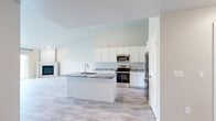 Located at 601 County U in Wrightstown, Wisconsin, this well-appointed single-floor unit offers a thoughtfully designed layout with one bedroom and one bathroom. The open-concept kitchen and living area serves as the heart of the home, featuring soaring ceilings that create an expansive, airy feel. The kitchen is outfitted with crisp white shaker cabinetry, granite countertops with elegant veining, a center island with an undermount sink, and a full suite of stainless steel appliances including a French door refrigerator, range, and microwave. Light wood-tone flooring flows throughout the entire unit, lending warmth and continuity to each room. The living area is anchored by a corner fireplace and benefits from generous natural light, with sliding glass doors opening to outdoor views of the surrounding greenery. A wall-mounted split system provides climate control alongside baseboard heating. The spacious primary bedroom features vaulted ceilings, a ceiling fan, a large window, and access to a dedicated closet. The bathroom includes white cabinetry, granite countertops, and tile flooring. Clean neutral tones and modern finishes throughout give this unit a fresh, move-in-ready appeal.