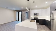 Located at 4201 S Navajo St in Englewood, Colorado, this single-floor unit showcases a clean, contemporary design throughout. The open-concept kitchen serves as a central highlight, featuring a large white quartz island with an undermount sink, a two-tone cabinet scheme pairing high-gloss white uppers with dark wood-grain lowers, and a full suite of stainless steel appliances including a refrigerator, range, and over-the-range microwave. A linear pendant light fixture above the island adds a modern, industrial accent, complemented by recessed lighting and under-cabinet illumination along the backsplash.

The living area extends seamlessly from the kitchen, finished with light wood-look luxury vinyl plank flooring that carries throughout the main living spaces. Black-framed glass sliding doors open to a private balcony, allowing natural light to fill the room. Bedrooms feature plush neutral carpeting, large windows, and ceiling fans, providing a comfortable and quiet retreat. A dedicated utility area is also present.

The bathroom is finished with large-format gray floor tiles, a glass-enclosed walk-in shower clad in white subway tile, and a modern vanity, delivering a spa-like aesthetic consistent with the unit's overall design sensibility.